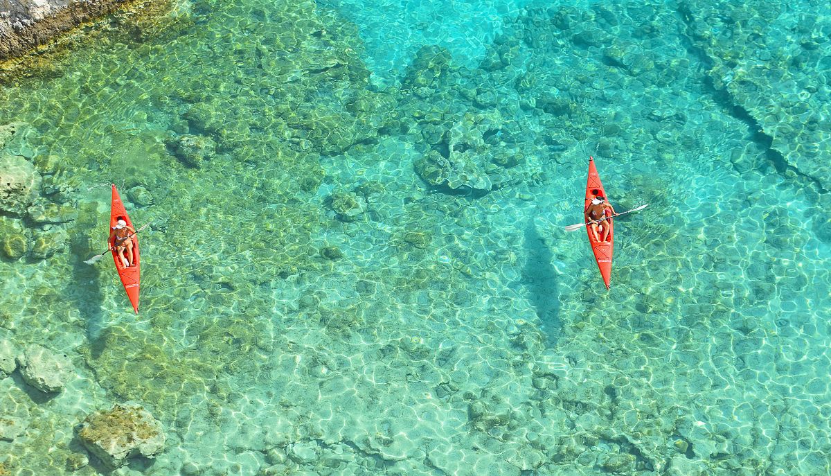 Couple enjoying kayaking in Barbados along crystal-clear turquoise waters with lush tropical coastline in the background.