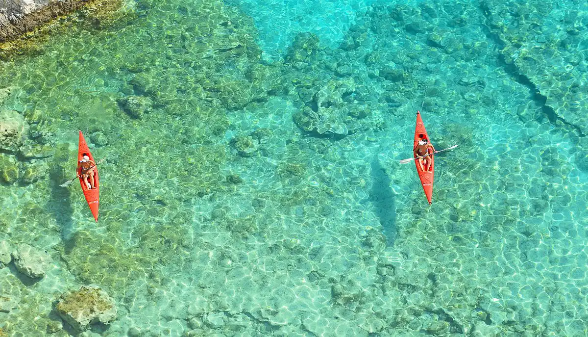 Couple enjoying kayaking in Barbados along crystal-clear turquoise waters with lush tropical coastline in the background.