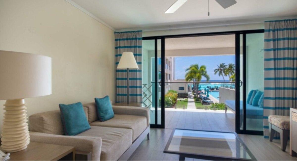 Bright living room at The Sands, Worthing, Christ Church, Barbados, with sliding doors opening onto a balcony overlooking the pool 